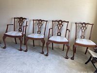 Four Chippendale style dining chairs with two armchairs and two side chairs arranged in a row, showing their carved backs and upholstered seats.