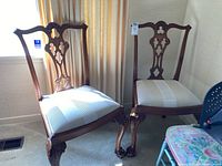Pair of Chippendale style mahogany chairs with carved splats and claw-and-ball feet, upholstered seats in striped fabric, minor scratches visible.