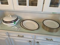 Covered soup tureen with lid alongside broken handle piece, two oval platters and stack of dinner plates
