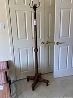 Full view of the wood coat tree with metal hooks in a room near doors and a chair.