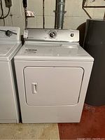 Front view of the white Maytag dryer showing door, control panel, and part of neighboring washer and water heater.