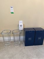 Two clear Mikasa glass vases, with original blue Mikasa boxes to the right of the vases, placed on a carpeted floor against a wall outlet.