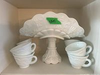Milk glass epergne with embossed grape and leaf design holding four stacked tea cups, measuring 12x9 inches