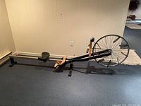 Full side profile of the rowing ergometer showing the metal rail, seat, footrests and large flywheel.