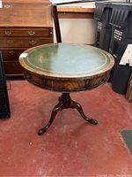 Full side view of the round wood table with green leather top and tripod legs.
