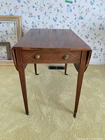 Front view of rectangular wooden table with drop leaves down, showing drawer and tapered legs with casters
