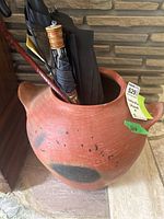 View of round terracotta umbrella stand with black spots and two handles, holding several umbrellas inside.