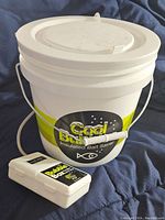 White insulated bait saver bucket with handle and lid labeled Cool Bubbles, placed on blue fabric background