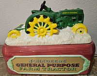 Side view of the green and yellow ceramic John Deere tractor cookie jar on a brown base with farm tractor sign.