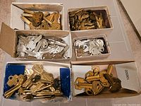 Multiple cardboard boxes filled with various vintage key blanks, mostly brass and silver, showing the quantity and packaging.