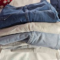 Top-down view of five pairs of vintage jeans in different denim washes stacked showing varied wear and fabric texture