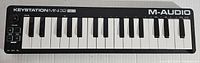 Full front view of the M-Audio Keystation Mini 32 MK3 keyboard showing all 32 keys, control buttons along the left side, and volume knob. A black compact design.