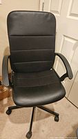 Front view of black office chair with padded seat and back, mounted on caster wheel base, with armrests.