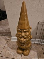 Full view of the ceramic garden gnome statue standing on tile flooring against a wall.