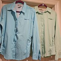 Two Columbia women's fishing shirts hanging on hangers, one light blue, one light green