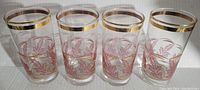 Four vintage mid century glasses with pink leaf designs and gold bands around the rim and base.