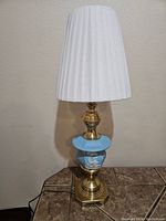 Full view of the vintage table lamp showing the white pleated lampshade, brass sections, and blue jasperware middle body with white relief design.