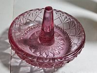 Top-down view showing pink glass ring holder with conical ring holder and textured rose/starburst pattern base.
