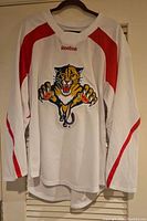 Full front view of white and red Reebok Florida Panthers hockey jersey on hanger.