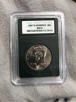 Front side of 1997-D Kennedy Half Dollar coin in protective case with certification label.