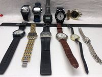 Lot of 11 wristwatches laid out on a fabric surface showing both digital and analog styles along with a gold-tone pocket watch.