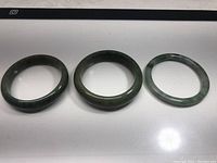 Three jade bracelets laid flat side by side showing their color variation and sizes.