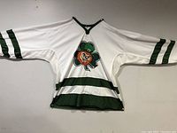 Front view of white hockey jersey shirt with green stripes and large four-leaf shamrock and leprechaun graphic