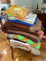 Stack of blankets and afghans folded on wooden chair, showing variety of colors and textures including crochet and solid fabrics.