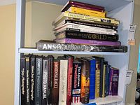Books stacked on shelves, showing titles mainly about photography, history, biographies, and fiction. Condition is worn with some shelf marks visible.