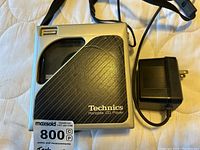 Front view of Technics portable CD player with charger showing model labeling and textured surface.