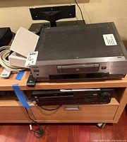 Front view of both units stacked on a wooden cabinet, Sony on top and Panasonic below
