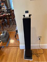 Full view of the tall black iCraig speaker with the white iPod resting on the dock on top and a black remote behind it.