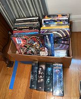 Overall view of the box containing various DVD titles stacked with some box sets visible on top and four DVDs/box sets outside the box on the floor