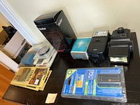 Photo showing assorted camera accessories on wooden surface including battery, flashes, filters, lens caps, and models grouped together