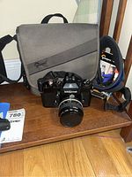 Nikkormat camera with attached Nikon lens placed on wooden surface with Lowepro bag behind it.