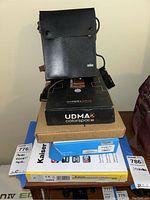 Stack of all items: Braun bag on top of UDMA2 box, plain brown box, Nanlite blue box, Kaiser white box