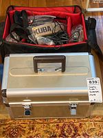Closed Hakuba aluminum gear case with brown handle and label identifying contents as empty case, batteries, and other items.
