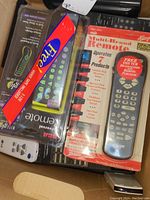 Box containing a mix of used and unused remote controls, some packaged including RCA and Mitchel Allegro.