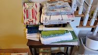 Stack of various towels and linens on small table including different colors and textures, some with fringed edges, showing worn condition.