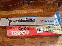 Boxed Manfrotto and Carrot video tripods stacked on hardwood floor