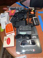 Full view of the lot items including boxes, devices, glasses, and cables spread on a table.