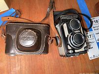 Yashica-44 camera with leather strap alongside Micronta 35X magnifier in a brown leather case, showing overall lot items.