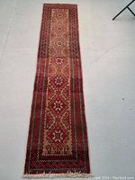 Full view of the Persian Balouch runner rug on the floor showing its multimedallion and border design with abrashed colors.