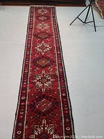 Full view of red geometric multi-medallion runner rug on white floor, tripod legs visible