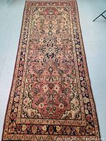 Full view top-down photo of the Persian rug showing its intricate floral central medallion and border pattern, in faded and varied hues due to vegetable dyes.