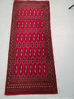 Full view of hand knotted Persian Turkman wool rug laid flat, showing rich red color and geometric pattern with borders.