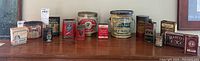 Wider shot showing all 15 tins, lined up on a wooden surface with various sizes and labels.