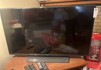 Front view of 48-inch Samsung Smart TV on wooden table with remotes in front.