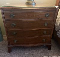 Front view of one wooden dresser with three drawers and metal oval pulls, glass top installed.