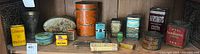 Shelf display showing 15 various antique lithographed food and spice tins including mustard and cocoa tins with visible wear and scratches.